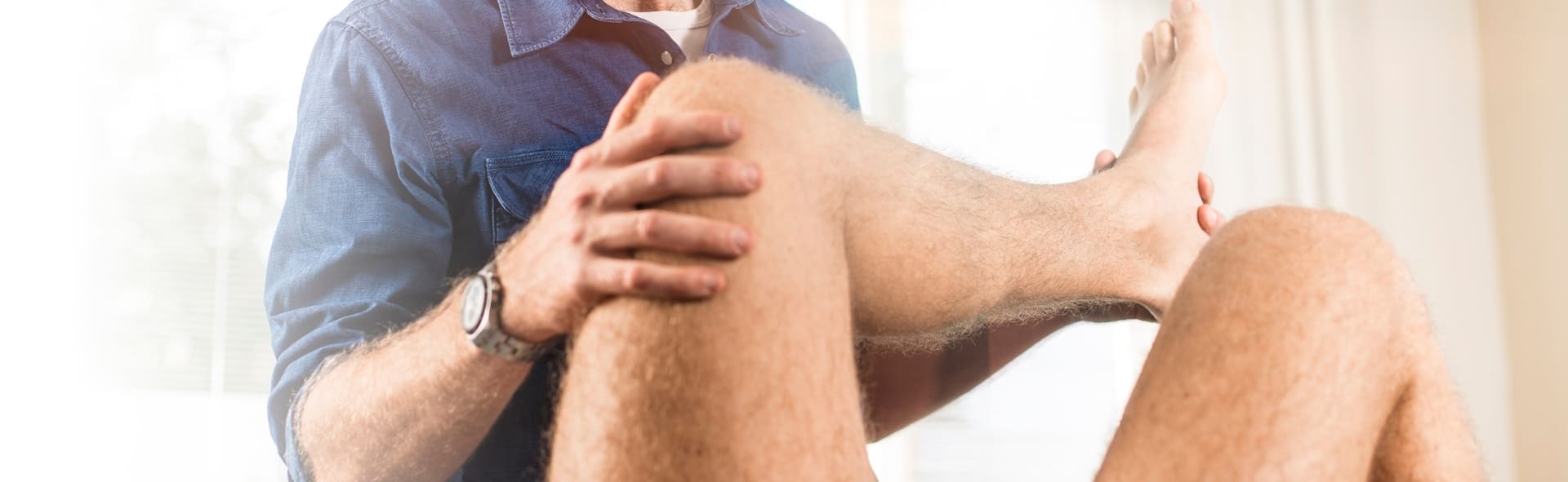 Fysiotherapeut buigt voorzichtig de knie van een patiënt op de behandeltafel.