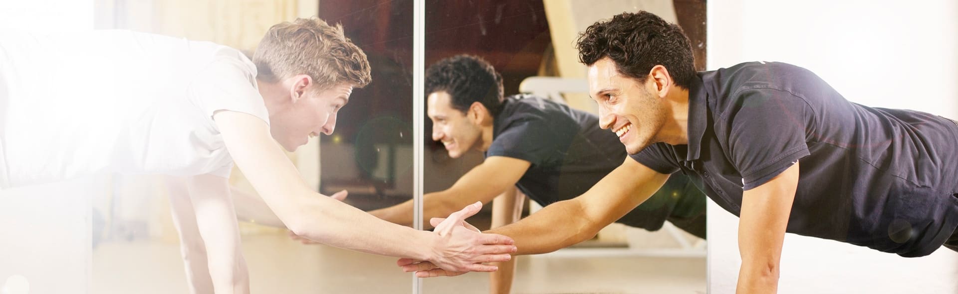 Twee mannen houden samen een plank vast in de oefenzaal en geven elkaar een hand.